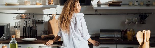 panoramische shot van meisje in wit shirt staande in de keuken - Foto, afbeelding