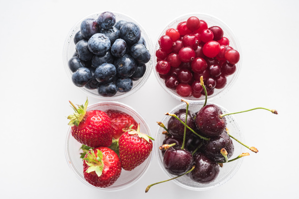top view of cranberries, strawberries, blueberries and cherries in plastic cups  - Фото, зображення