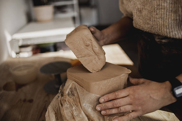 Женщина гончар работает с глиняными осколками, ремесленник закрывает руки, разминает и увлажняет глину перед работой, тонизирует. Производство, посуда ручной работы
  - Фото, изображение