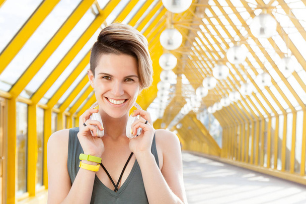 Jovem mulher positiva em fones de ouvido está sorrindo em pedestres indoor
 - Foto, Imagem