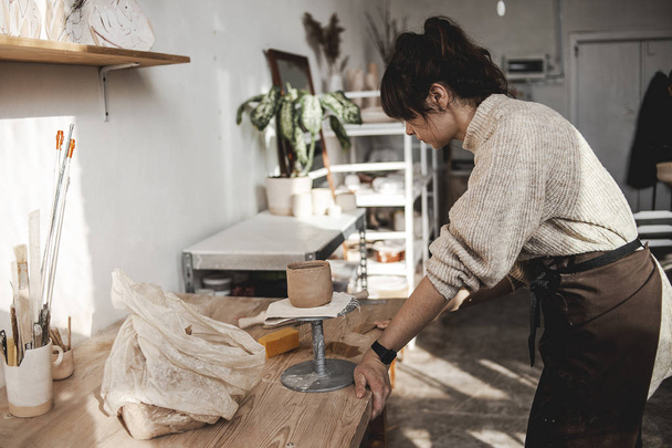 Професійна жінка-гончарка на своїй творчій художній студії в процесі створення і моделювання нового глиняного посуду ручної роботи або чогось для інтер'єру. Творча професія, виробництво. Мистецький простір
 - Фото, зображення