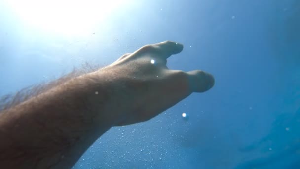 De mannelijke hand strekt zich uit van onder water tot zonnestralen. Arm vraagt om hulp en probeert naar de zon te reiken. Het standpunt van de mens die verdrinkt in de zee of oceaan en naar de oppervlakte drijft. Slow motion POV - Video