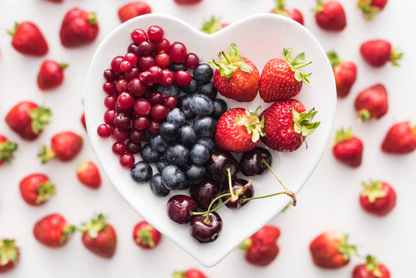 top view of sweet cranberries, blueberries, strawberries and cherries on heart shaped plate  - Zdjęcie, obraz