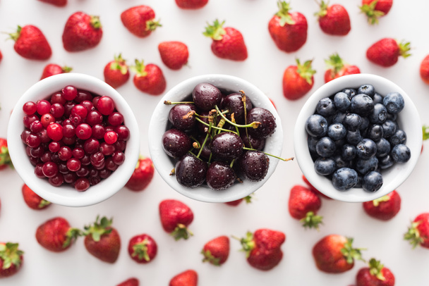top view of sweet blueberries, cherries and cranberries on bowls and strawberries on background  - Photo, Image
