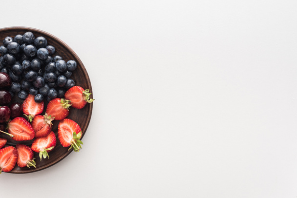 top view of sweet blueberries, cherries and cut strawberries on plate  - Zdjęcie, obraz