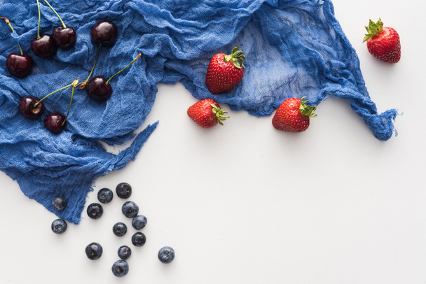 top view of sweet blueberries, cherries and whole strawberries on blue cloth  - Foto, afbeelding