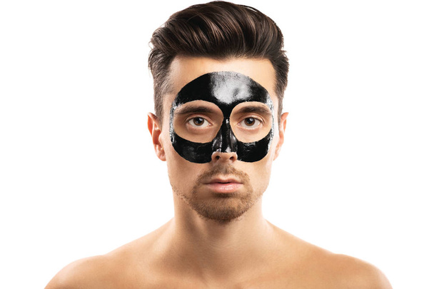 Young guy with a black charcoal mask on his face on white backgr - Фото, зображення