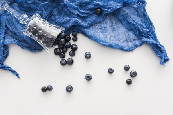 top view of sweet and ripe blueberries and wine glass on blue cloth  - Photo, Image