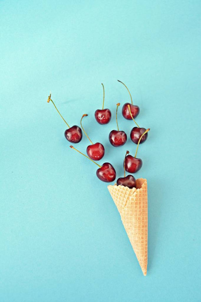 Конус мороженого, полный вишни, на фоне яркого фона, как символ фруктового освежения летом
 - Фото, изображение