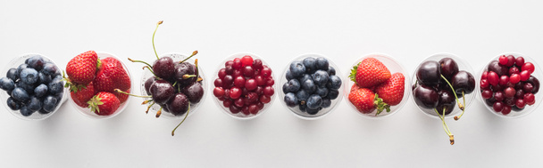 panoramic shot of fresh and ripe strawberries, blueberries, cherries and cranberries in plastic cups  - Foto, Imagem