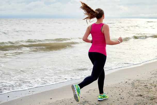Back view of athletic woman running on sea beach, copy space. Fe - Photo, Image