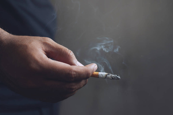 Человек, который курит сигарету в руке. Сигаретный дым распространился. темный фон
 - Фото, изображение
