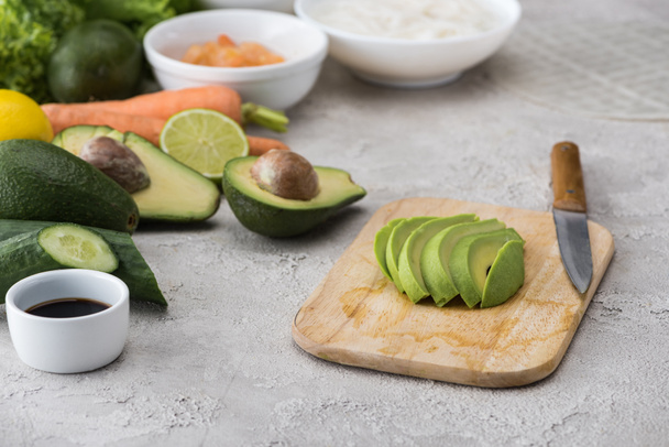 cut avocado on cutting board with knife among raw ingredients  - Φωτογραφία, εικόνα