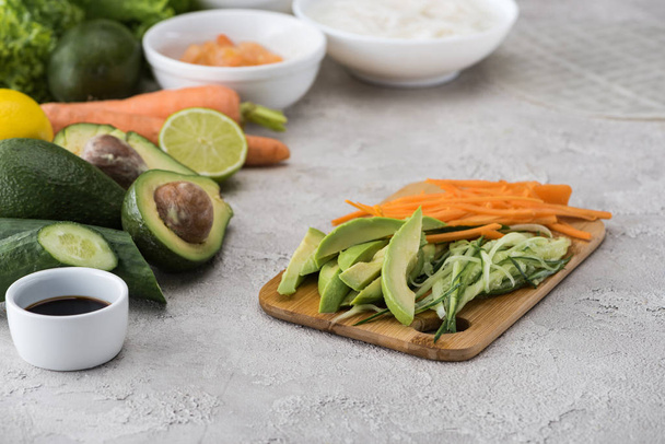 cut avocado, carrot and cucumber on cutting board among raw ingredients  - 写真・画像