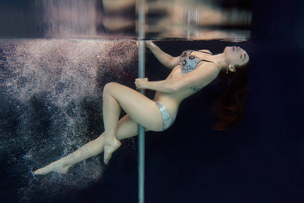 Young, fit, slim woman in swimming crystal bra and underpants with pole underwater in the swimming pool on black background - Fotoğraf, Görsel