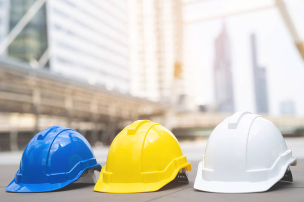 żółty, niebieski i biały kask twardy bezpieczeństwa nosić kapelusz w projekcie na budowie budynku na betonowej podłodze w mieście. Kask dla robotnika jako inżynier lub pracownik. koncepcja bezpieczeństwa pierwszy - Zdjęcie, obraz
