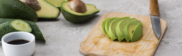 panoramic shot of cut avocado on cutting board with knife among raw ingredients  - Photo, Image