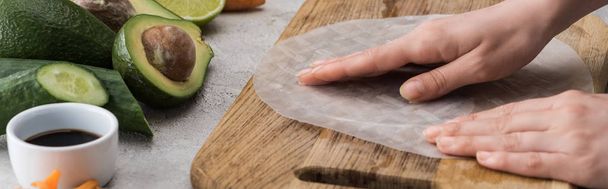 plan panoramique de femme mettant du papier de riz sur planche à découper parmi les ingrédients
  - Photo, image