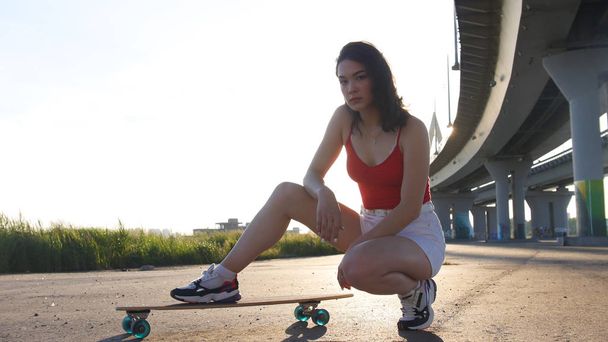 Jeune femme séduisante assise sur le skateboard sous le pont
 - Photo, image