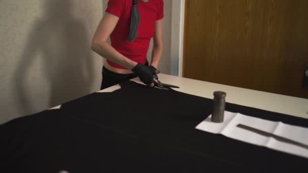 Cyber punk fashion designer at work in her studio cutting pattern - Caucasian white woman wearing red t-shirt and black gloves with scissors hanging over her chest - Video, Çekim