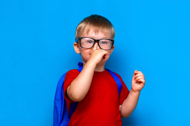 Маленький улыбающийся школьник на синем фоне в очках подбирает очки. Назад в школу, ребенок дошкольного возраста
 - Фото, изображение