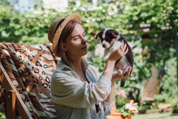 rubia chica en paja sombrero celebración galés corgi cachorro mientras sentado en cubierta silla en jardín
 - Foto, Imagen