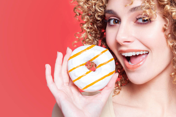 Beautiful young cheerful girl bites donut - Фото, изображение