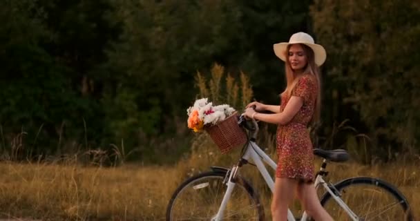 Oldalnézet: mosolygó lány egy ruhában séta a kerékpáros a nyáron a kormány kosár vadvirágok. - Felvétel, videó