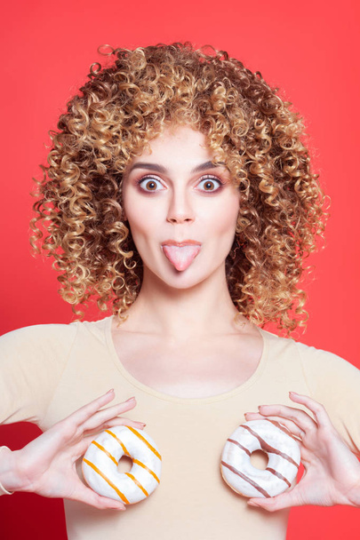 Beautiful young cheerful girl shows tongue and holds donuts in f - Photo, Image