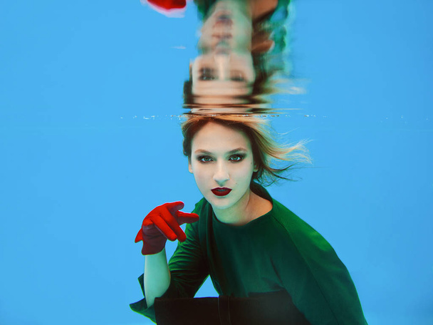 mooie geweldige stijlvolle mooie jonge vrouw in groene jurk, rode handschoenen, zwarte Clutch tas en panty's in het net onder water in het zwembad. Mode en Shopping concept - Foto, afbeelding