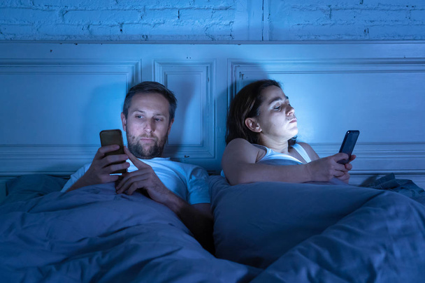 Couple affected by technology addiction ignoring at each other in apathy and anger lying in bed using their smart phones late at night in darkness in relationship issues and internet mobile addiction. - Fotó, kép