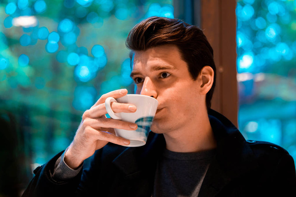 Handsome man drinking tea or coffee on rainy day and looking through the window - Zdjęcie, obraz