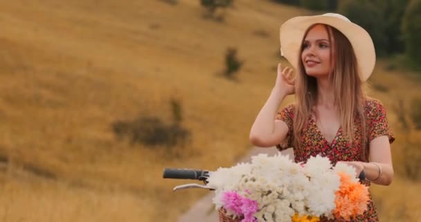 Porter chica caminando en cámara en un vestido con flores en una cesta y una bicicleta en el campo
. - Metraje, vídeo