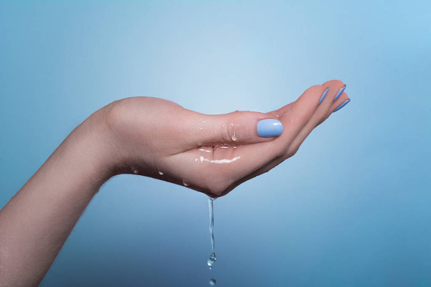 A picture of a woman's hand on which water flows, on a blue background - Photo, image