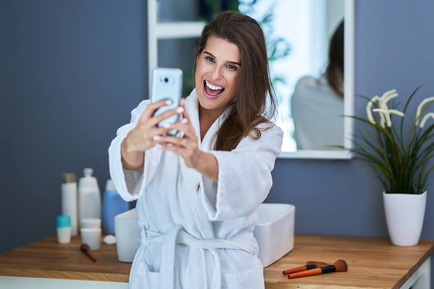 Mooie brunette vrouw met Smart Phone in de badkamer - Foto, afbeelding