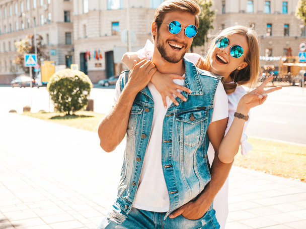 Smiling beautiful girl and her handsome boyfriend. Woman in casual summer dress and man in jeans clothes. Happy cheerful family. Female having fun on the street background.Hugging couple in sunglasses - 写真・画像