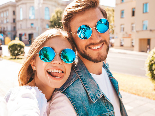 Smiling beautiful girl and her handsome boyfriend in casual summer clothes.Happy family taking selfie self portrait of themselves on smartphone camera in sunglasses.Having fun on the street background - Foto, Imagem