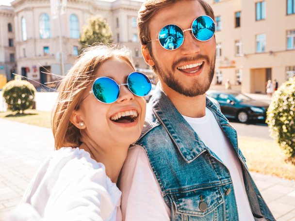 Smiling beautiful girl and her handsome boyfriend in casual summer clothes.Happy family taking selfie self portrait of themselves on smartphone camera in sunglasses.Having fun on the street background - Zdjęcie, obraz