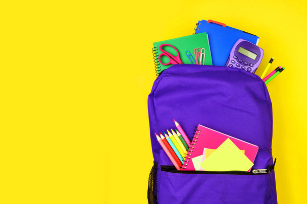 Mor sırt çantası parlak sarı bir arka plan karşı okul malzemeleri dolu. Kopyalama alanı ile yukarı, üst görünüm. - Fotoğraf, Görsel