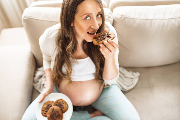 Top view of pregnant woman eating cookies for breakfast. Looking at camera - Foto, Imagem