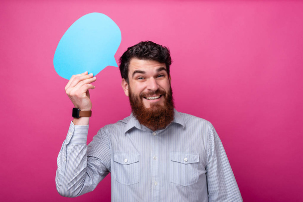 Laissez un commentaire ! Jeune homme barbu tient une bulle de discours bleu sur fond rose
. - Photo, image
