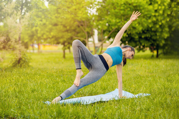 Młoda kaukaska kobieta uprawia jogę w parku. - Zdjęcie, obraz