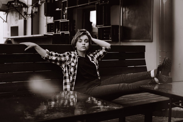 Young woman with short hair in a bar put her legs on table - Фото, зображення