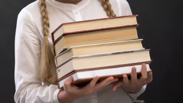 Schoolgirl in eyeglasses holding books against blackboard, education, geek - Filmati, video
