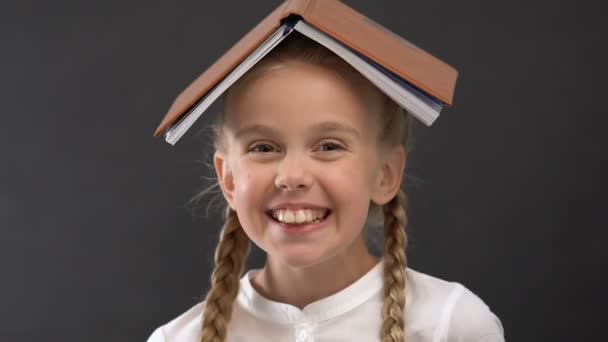 Pretty schoolgirl with book on head laughing and fooling around, childish mood - Кадры, видео