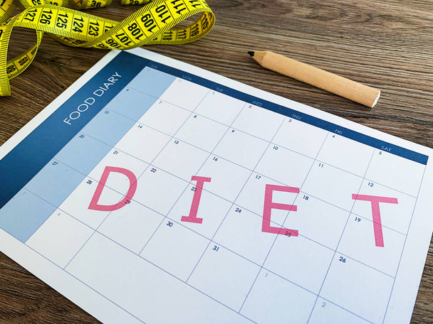 Diet plan concept. Measuring tape and diet plan on wooden background. - Photo, Image