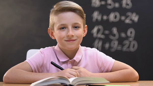 Αγόρι κάθεται στο σχολικό γραφείο κατά τη διάρκεια του μαθήματος μαθηματικά και κοιτάζοντας την κάμερα, εκπαίδευση - Πλάνα, βίντεο