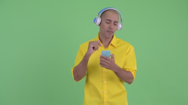 Happy handsome bald businessman using phone and listening to music - Filmagem, Vídeo