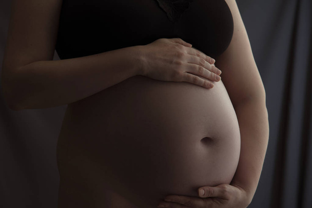 Pregnant woman holding a baby bump against a dark background - Foto, afbeelding