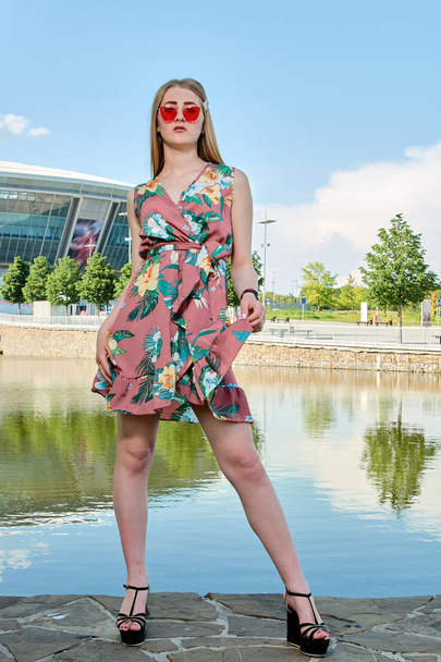 Young attractive woman. Red sunglasses, color dress. Girl's portrait. Football stadium background. - Photo, Image